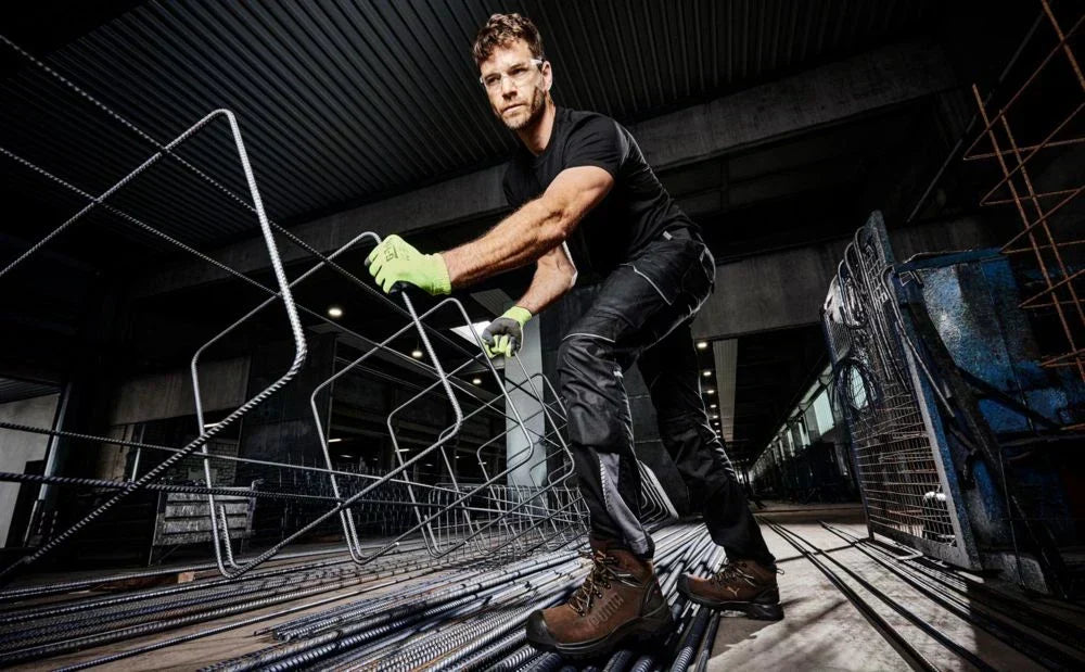Sicherheitsschuh "Iron HD" von Puma Safety im Einsatz auf einer Baustelle – ein Mann hantiert mit Bewehrungsstahl, trägt dunkle Arbeitskleidung und neongrüne Schutzhandschuhe von G-Tek.