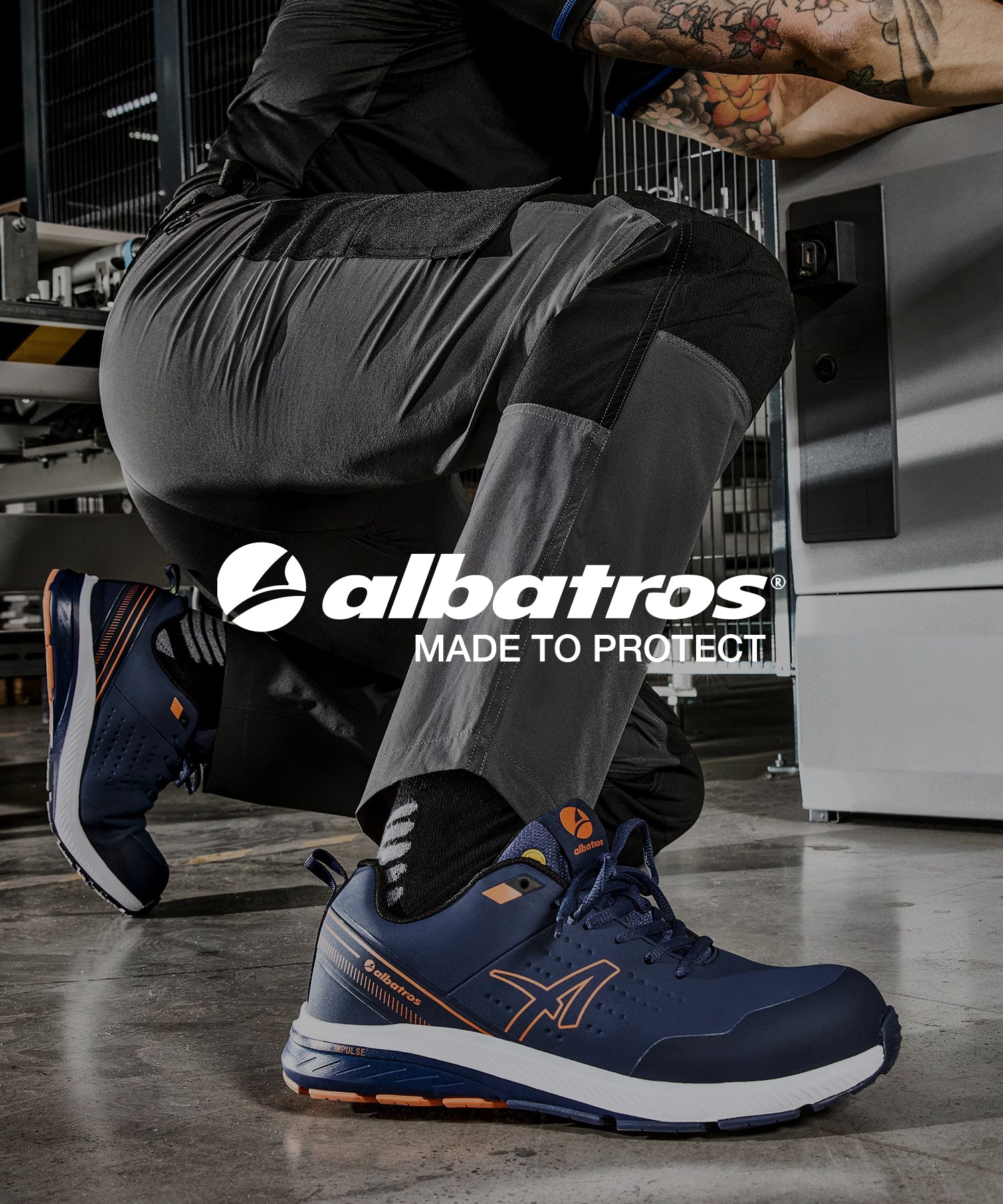 Arbeiter kniet auf einem Industriehallenboden und trägt den dunkelblauen Sicherheitsschuh "Vigor 2 Impulse" von Albatros mit orangen Details.
