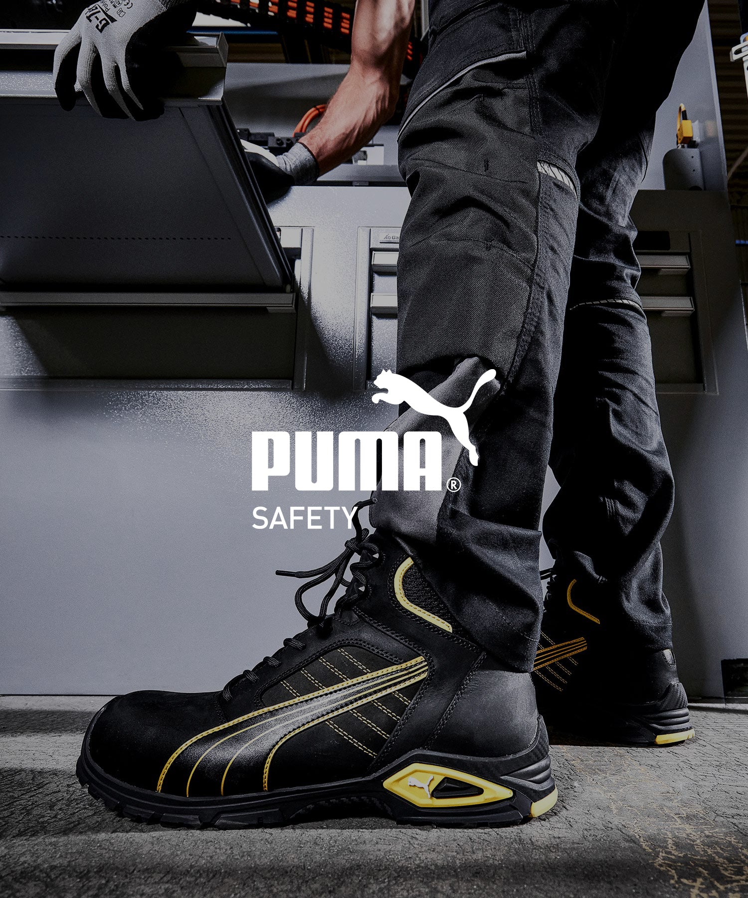 Arbeiter steht vor einer Industriemaschine und trägt den schwarzen Sicherheitsschuh "Amsterdam von Puma Safety mit gelben Akzenten.