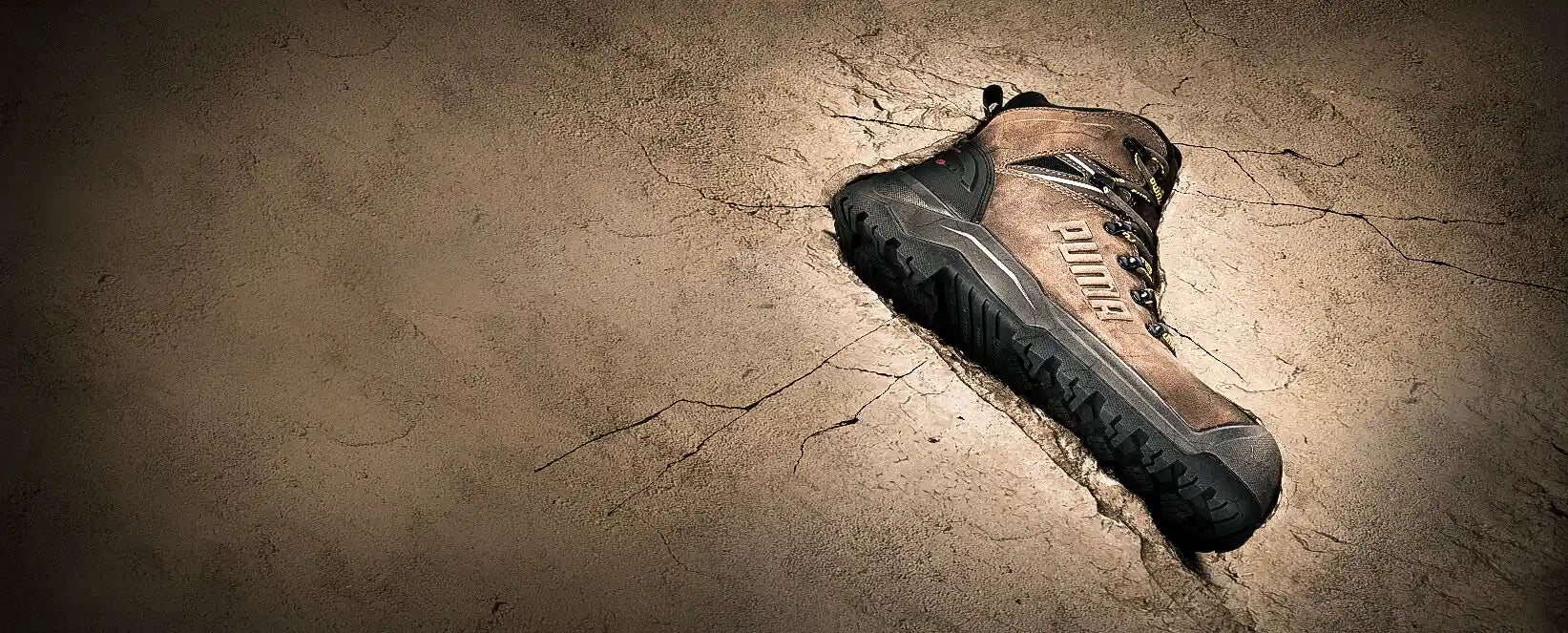 Sicherheitsschuhe "Iron HD" von Puma Safety in Braun mit robuster Laufsohle - Arbeitsschuh auf rissigem, steinähnlichem Untergrund inszeniert.