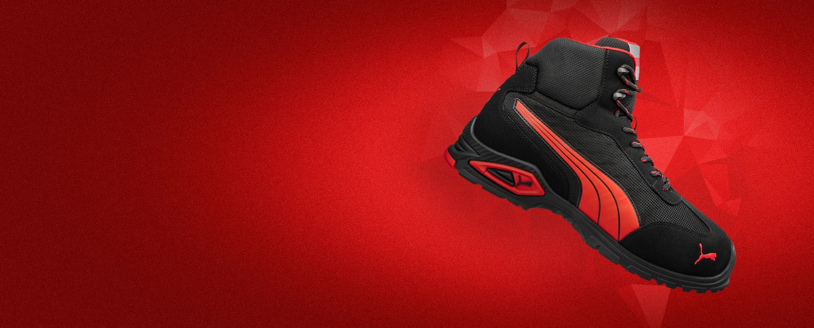 Sicherheitsschuh "Madrid" von Puma Safety in Schwarz mit roter Sohle und markantem Designelement- sportlicher High-Top-Arbeitsschuh vor dynamischem roten Hintergrund.