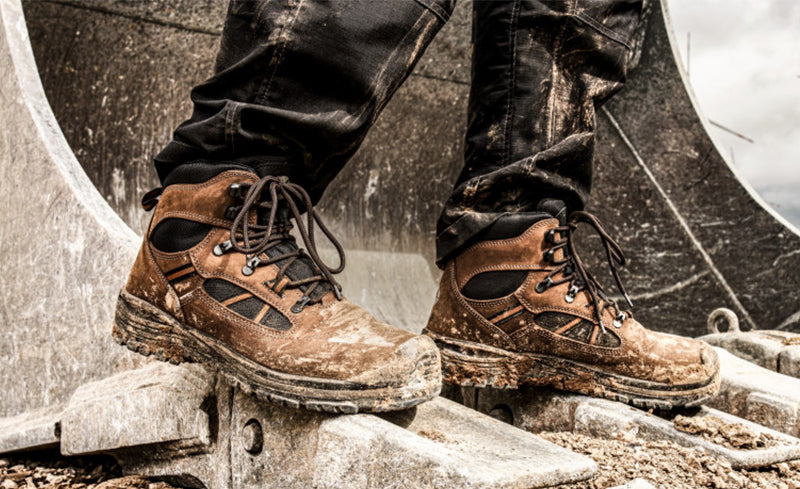 Verschmutzter, robuster Sicherheitsstiefel "Timber" von Albatros im Einsatz auf einer Baustelle – stehend auf der Schaufel eines Baggers.