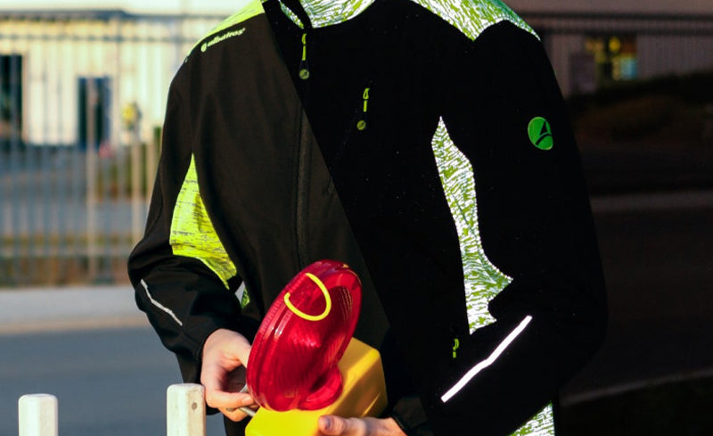 Person in Arbeitsjacke von Albatros mit reflektierenden Elementen – links bei Tageslicht, rechts bei Dunkelheit mit Reflektionseffekt – hält rote Warnleuchte in den Händen.