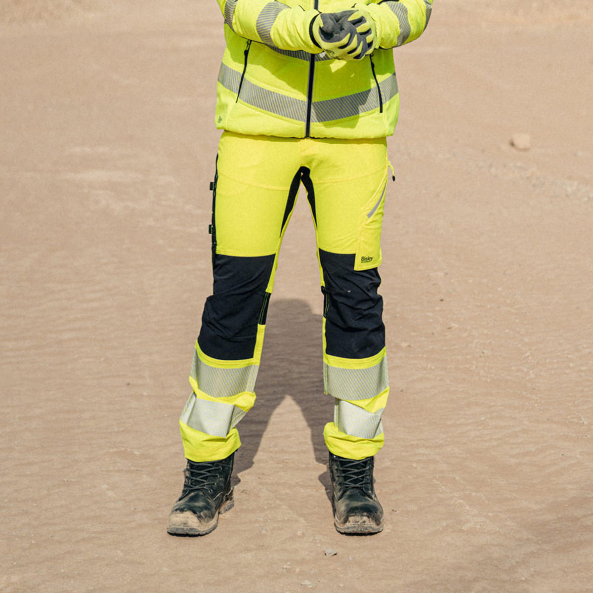 Mann mit BISLEY BRADFORD HI VIS Arbeitshose gelb auf Sand