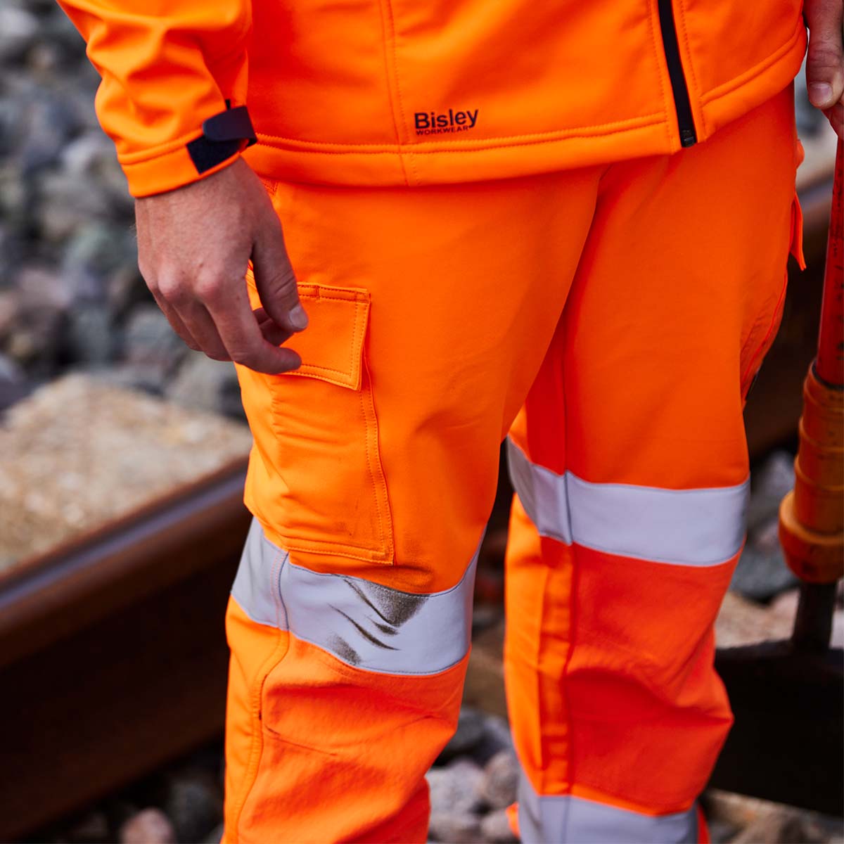 Arbeiter in oranger Bisley Warnschutz-Arbeitskleidung mit reflektierenden Streifen – robuste Schutzbekleidung für Baustelle, Gleisbau und Handwerk.