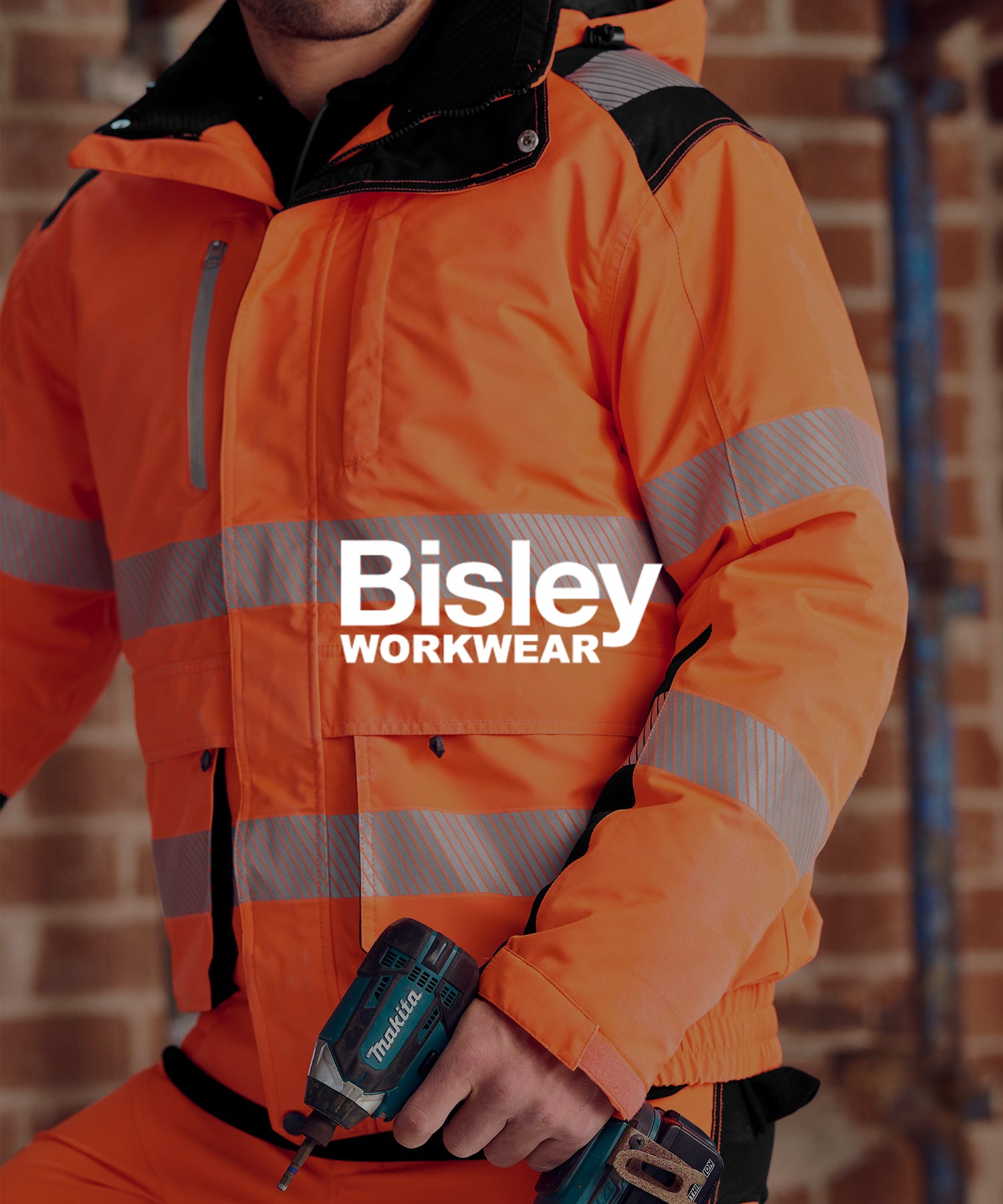 Handwerker in leuchtend orangefarbener HI VIS Warnschutzjacke von Bisley mit reflektierenden Streifen, hält eine Makita-Akkubohrmaschine vor einer Ziegelwand.