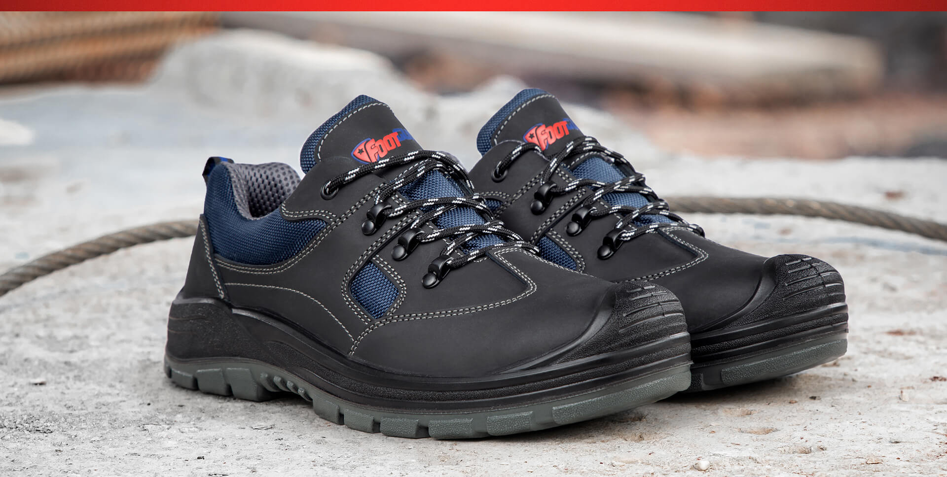 Sicherheitsschuh "Safe" von Footguard in Schwarz mit blauem Mesh-Einsätzen, stehend auf hellem Betonboden.