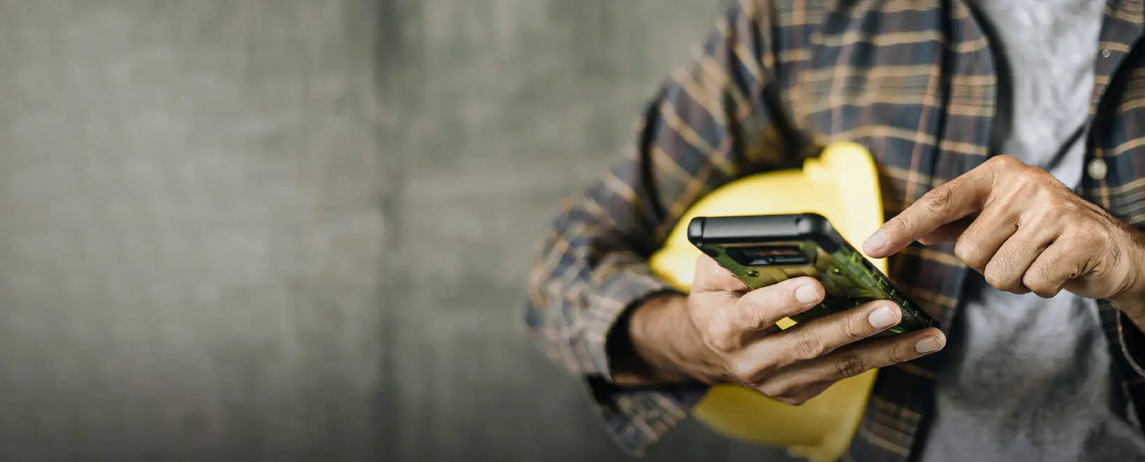 Bauarbeiter mit kariertem Hemd und gelben Schutzhelm nutzt Smartphone - modernes Handwerker-Influencer-Konzept.