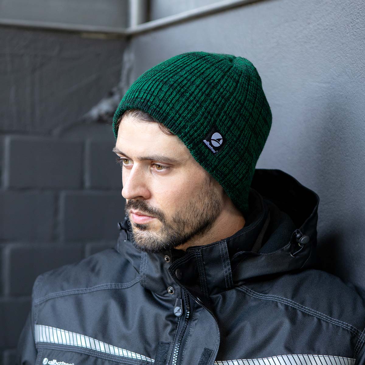 Mann mit grüner Strickmütze und schwarzer Arbeitsjacke von Albatros vor einem grauen Hintergrund.