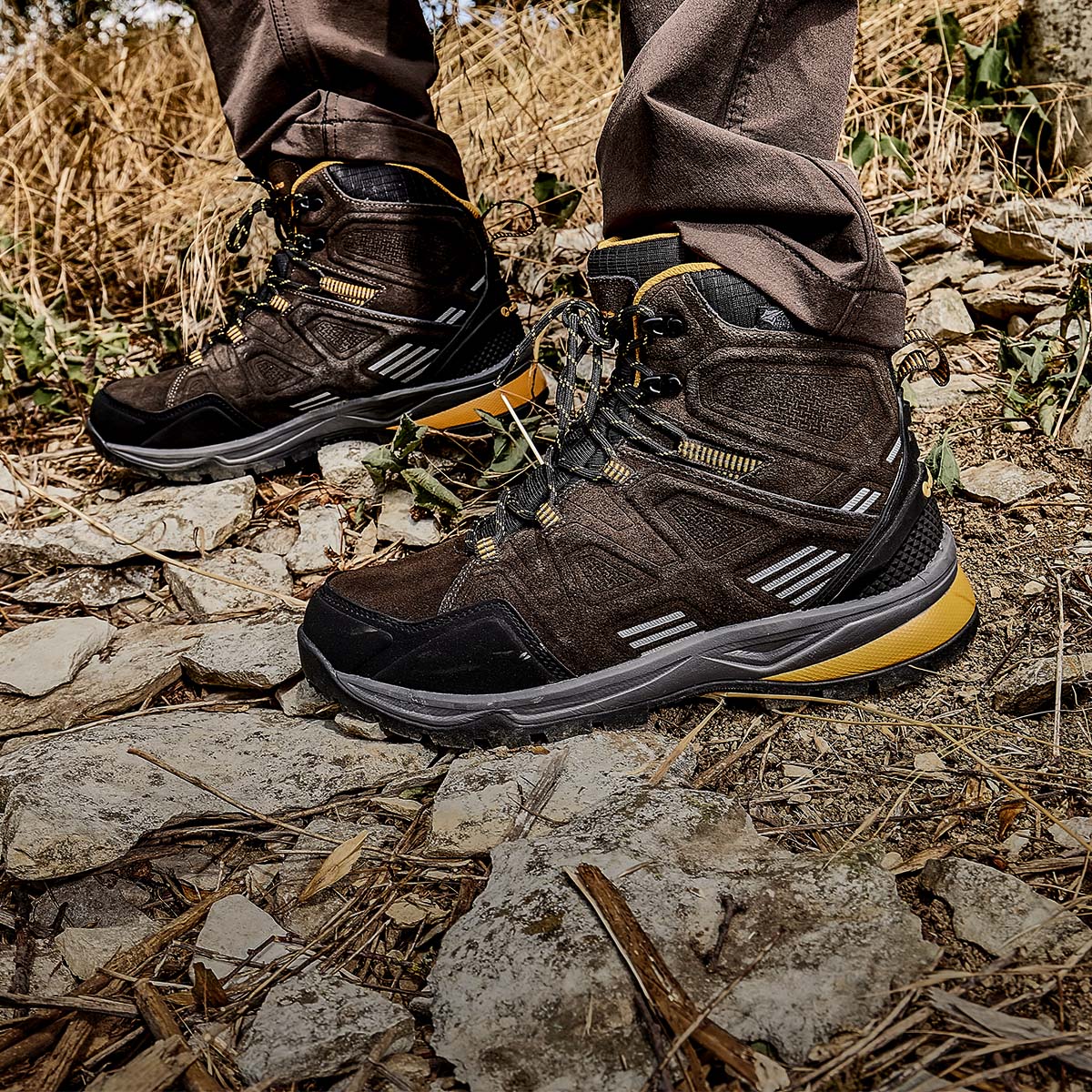 ALBATROS® Trekkingschuhe in Dunkelbraun mit gelben Details und grob profilierter Sohle, getragen auf einem steinigen Outdoor-Untergrund.