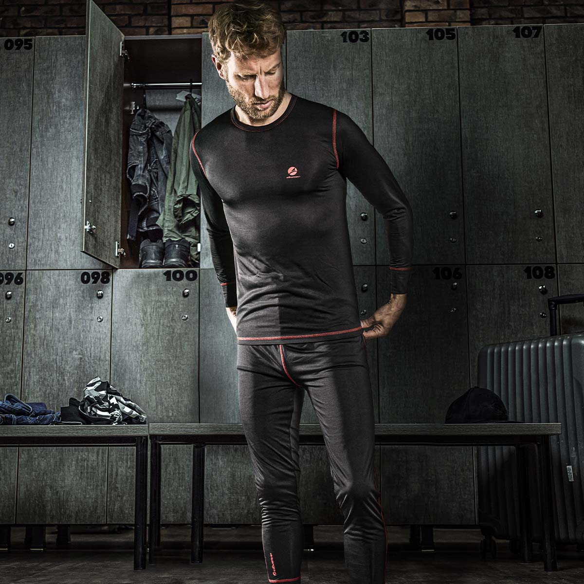 Mann in schwarzer Funktions- und Thermounterwäsche von Albatros mit roten Nähten beim Umziehen in einer Umkleide - eng anliegende, atmungsaktive Arbeitsunterwäsche für kalte Einsätze.