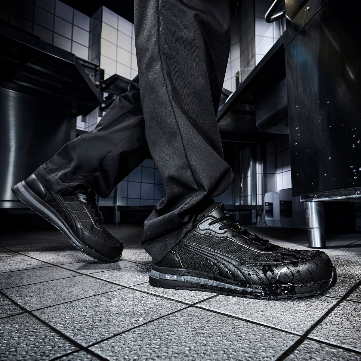 Rutschfester Arbeitsschuh "Epic" von Puma Safety in Schwarz, getragen auf nassem Küchenboden.