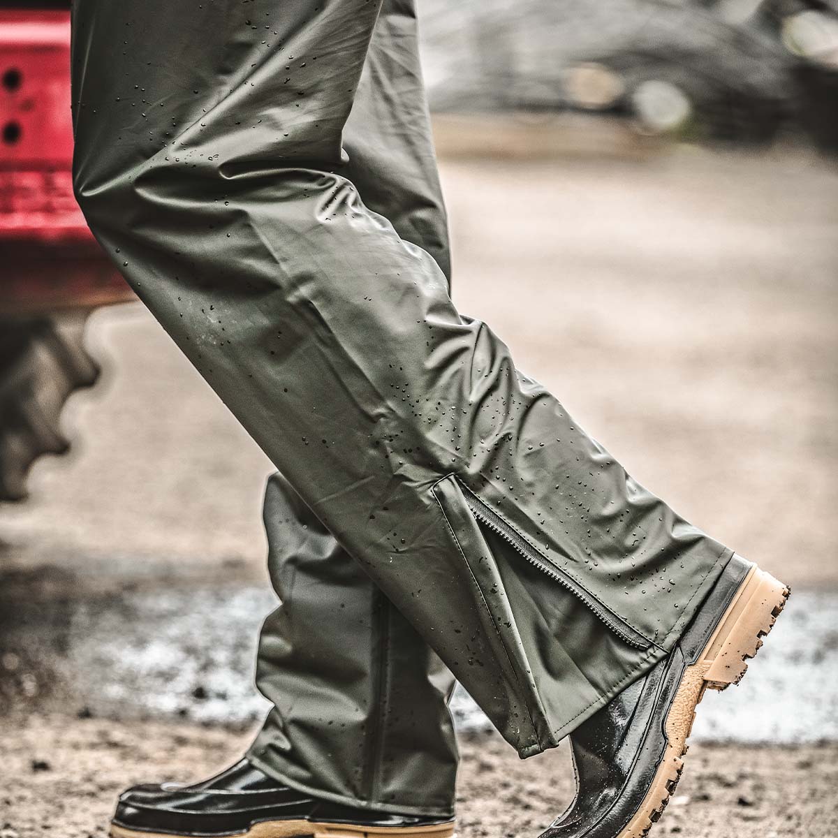 Wasserabweisende grüne Regenhose mit Reißverschluss am Beinabschluss, getragen über Gummistiefel - Einsatz im Outdoorbereich bei Nässe.
