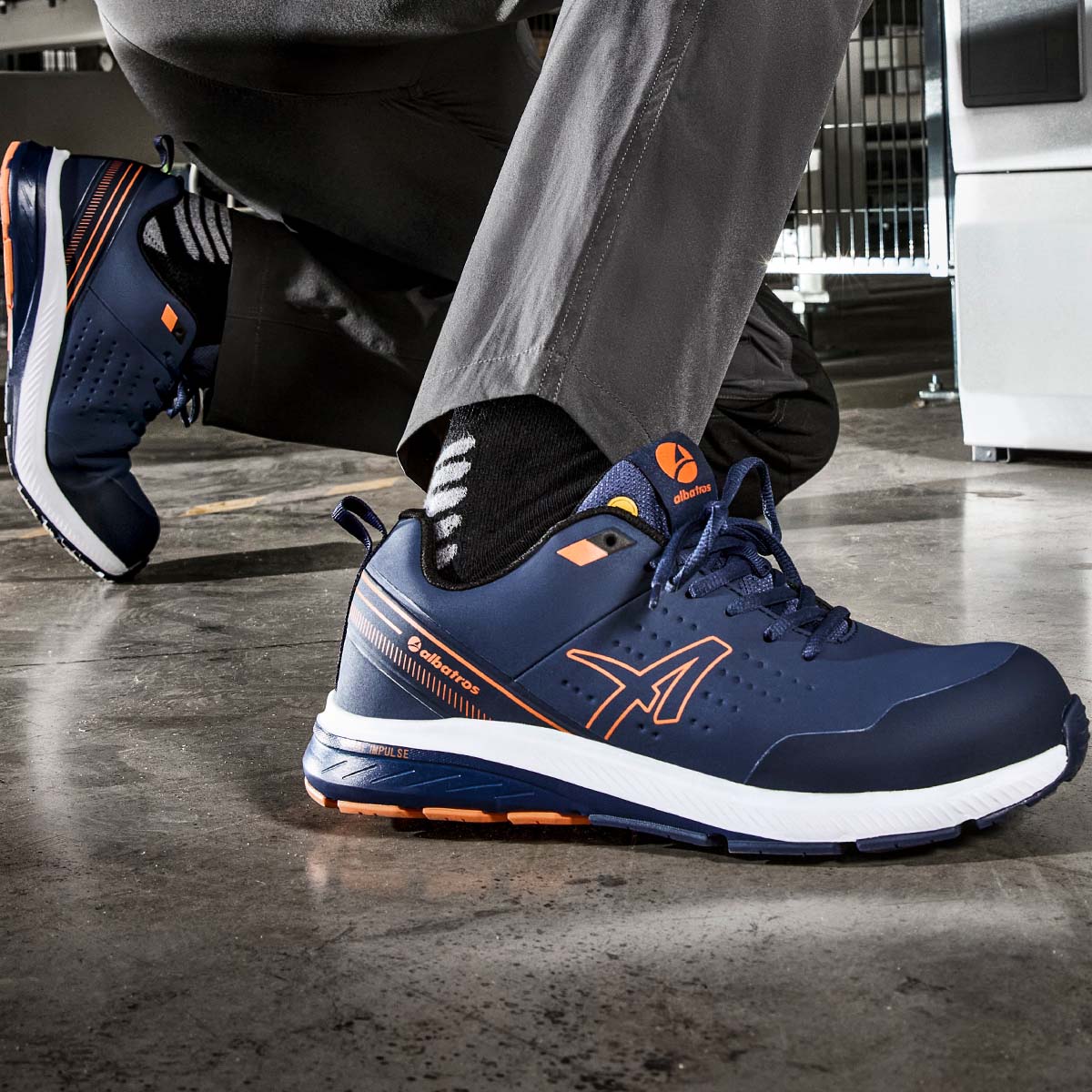 Blauer Halbschuh mit orangefarbenen Details der Marke ALBATROS®, getragen auf glänzendem Industriehallenboden.