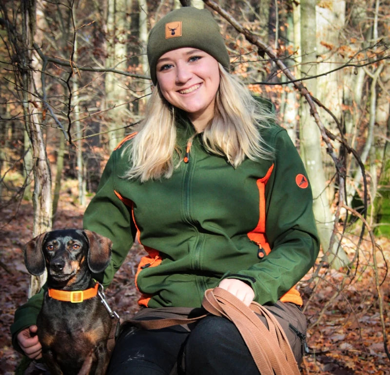 Die Influencerin Maya hockt in im Wald gemeinsam mit ihrem Dackel. Dabei trägt sie eine grüne Softshelljacke von Albatros.