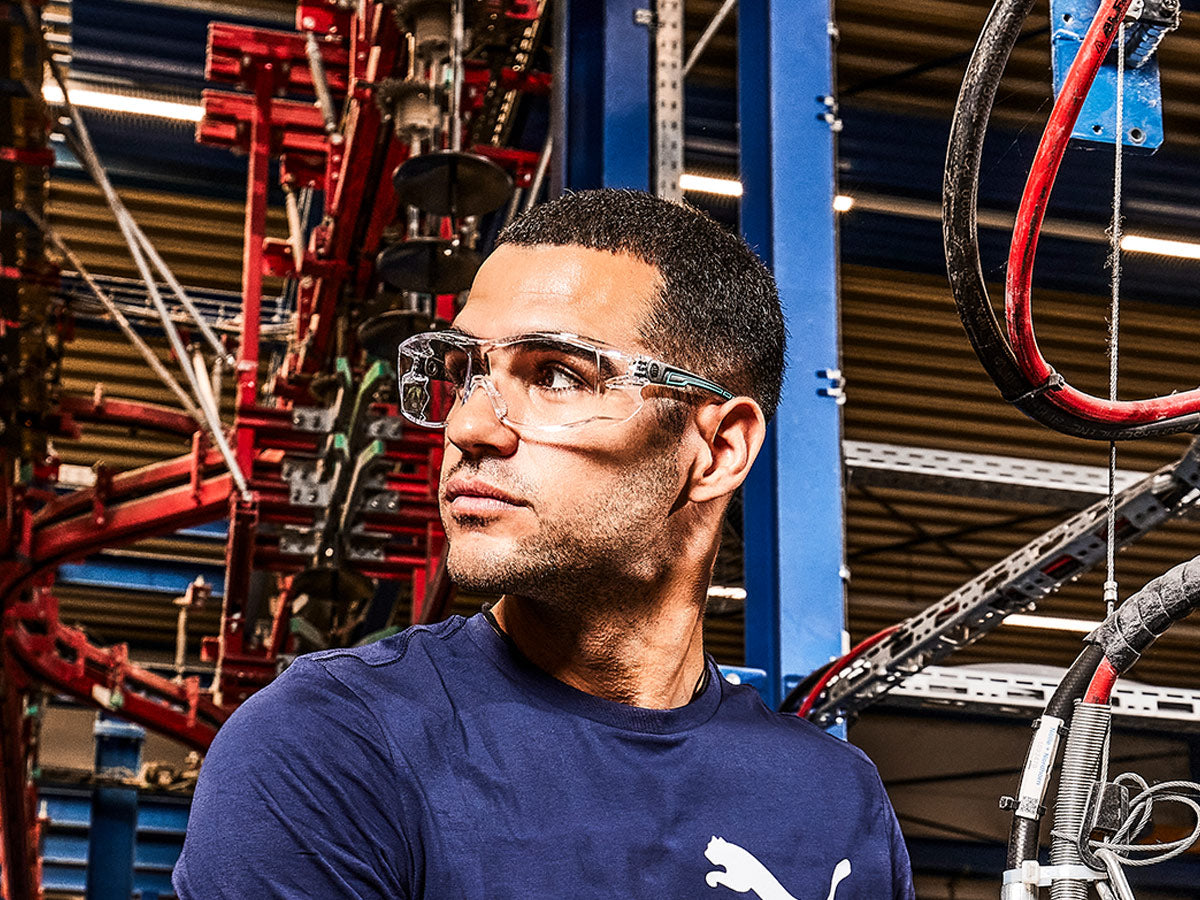 Mann mit transparenter Schutzbrille in industrieller Umgebung - PSA für sicheren Augenschutz.