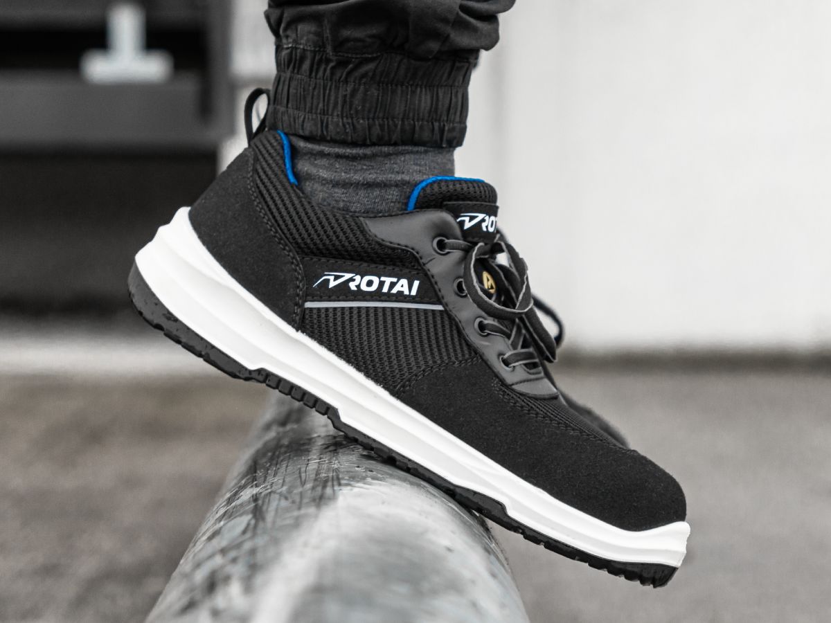 Sicherheitsschuh "RS PRO 22" von Rotai in Schwarz mit weißer Sohle, getragen auf einem Geländer.